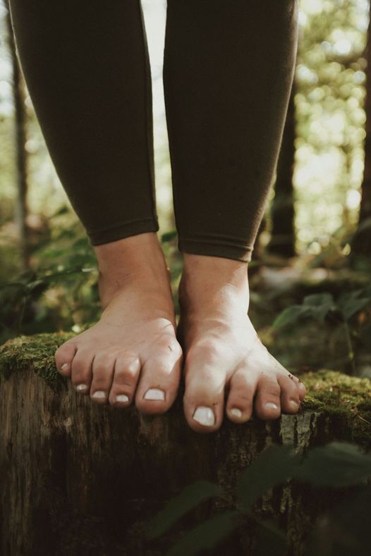 Des pieds nus posés sur un tronc en forêt, en cadrage serré.